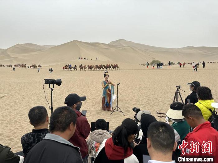 圖為2023年4月底，敦煌大漠“逐舞者”奧楠在鳴沙山月牙泉景區(qū)視頻直播，吸引游人圍觀?！●T志軍 攝